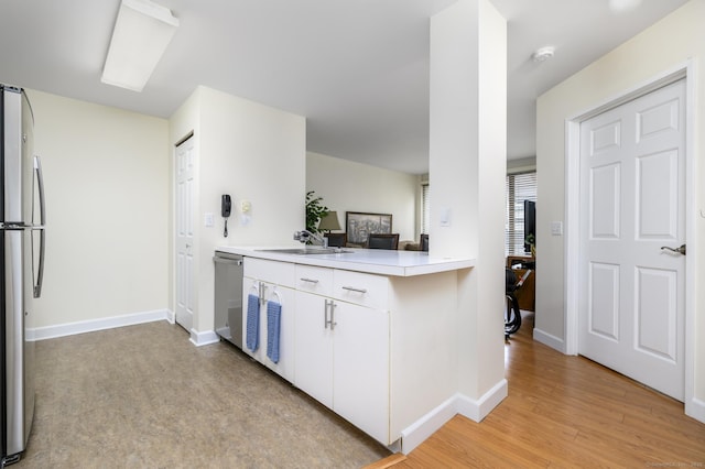 kitchen featuring stainless steel appliances, a sink, white cabinetry, light countertops, and light wood finished floors