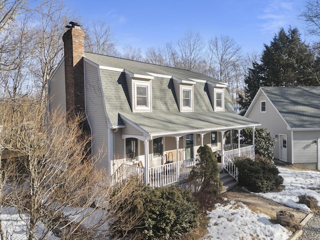 colonial inspired home with covered porch, roof with shingles, a chimney, and a gambrel roof