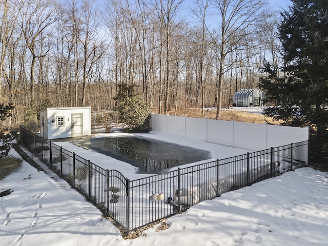 snow covered pool with a fenced backyard, a storage unit, a fenced in pool, and an outbuilding