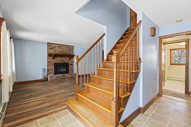 stairs with baseboard heating, a fireplace, wood finished floors, and baseboards