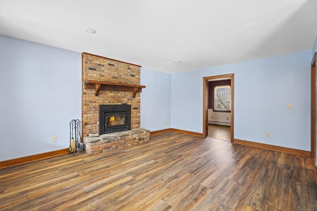 unfurnished living room with a baseboard heating unit, a fireplace, wood finished floors, and baseboards