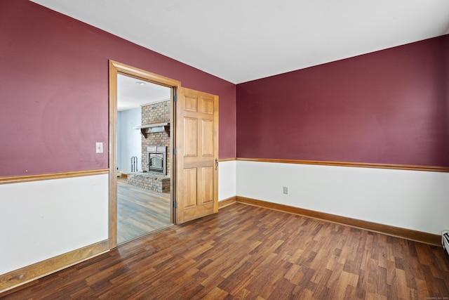 unfurnished room featuring a brick fireplace, baseboards, and wood finished floors