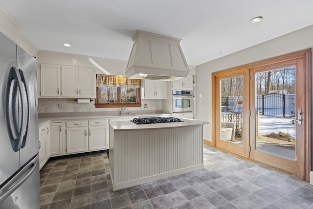 kitchen with tasteful backsplash, custom range hood, a kitchen island, stainless steel appliances, and light countertops