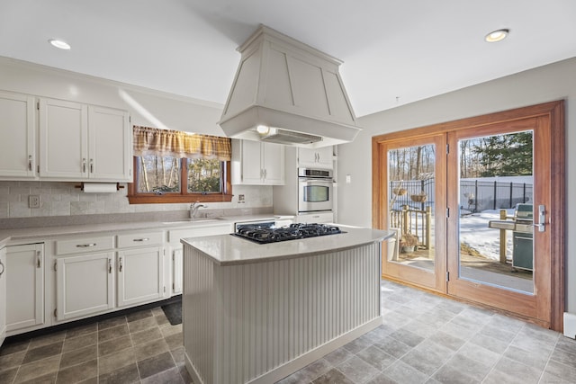 kitchen featuring light countertops, custom range hood, decorative backsplash, a sink, and black gas stovetop