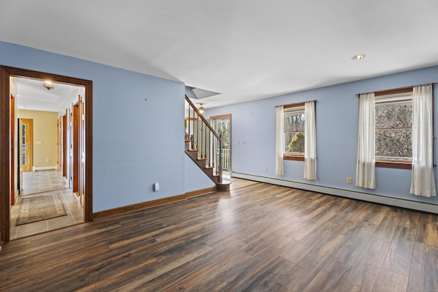 empty room featuring a baseboard radiator, stairway, baseboard heating, wood finished floors, and baseboards