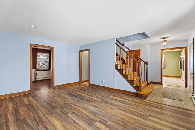 spare room with a baseboard heating unit, wood finished floors, baseboards, and stairs