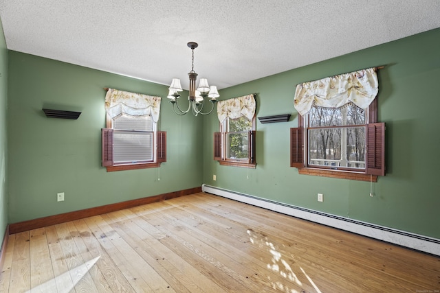 empty room with hardwood / wood-style floors, baseboard heating, an inviting chandelier, a textured ceiling, and baseboards