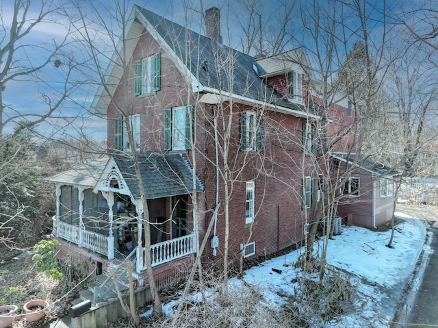 view of snowy exterior featuring brick siding and a chimney