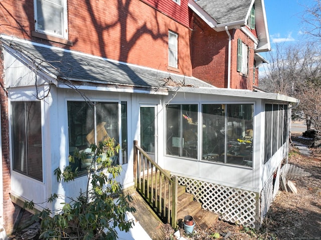 view of property exterior with a shingled roof, entry steps, a sunroom, and brick siding