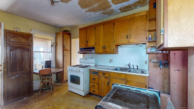 kitchen featuring white gas stove, light floors, brown cabinetry, a sink, and under cabinet range hood