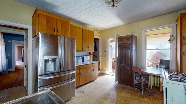 kitchen featuring stainless steel refrigerator with ice dispenser, light floors, light countertops, brown cabinetry, and white range with gas cooktop