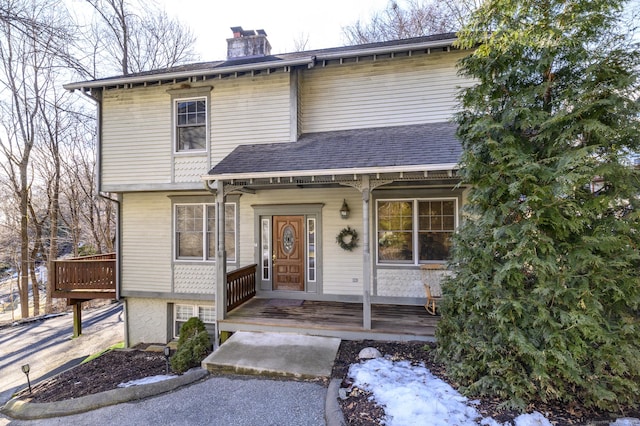 view of front of property with covered porch, a shingled roof, and a chimney