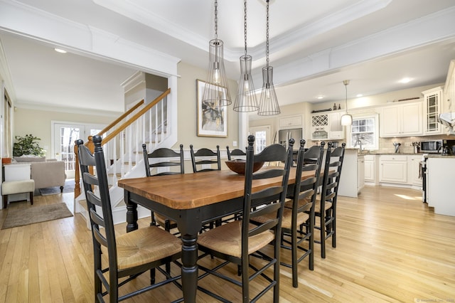 dining space featuring stairs, a tray ceiling, light wood finished floors, and crown molding