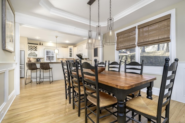 dining room featuring light wood-style floors, a tray ceiling, crown molding, and wainscoting