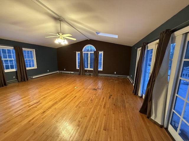 interior space with a ceiling fan, vaulted ceiling with skylight, baseboards, and hardwood / wood-style floors