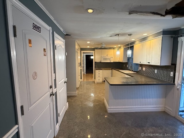 kitchen featuring white microwave, a peninsula, a sink, decorative backsplash, and dark countertops