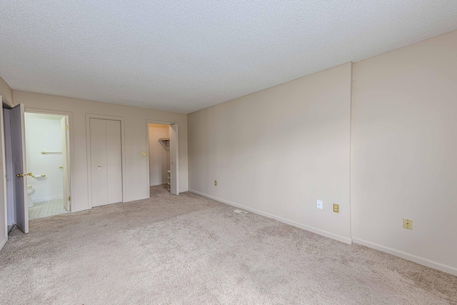 unfurnished bedroom featuring baseboards, connected bathroom, a spacious closet, a textured ceiling, and carpet flooring