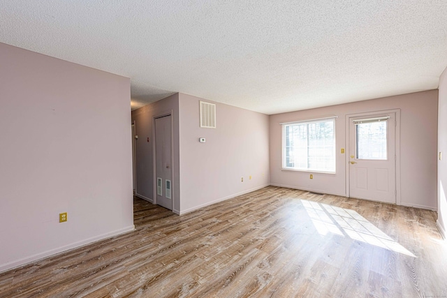 empty room featuring a textured ceiling, visible vents, and wood finished floors