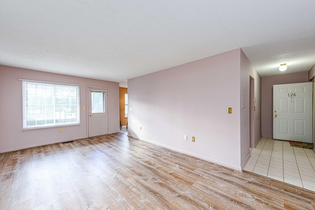 empty room with light wood-type flooring, baseboards, visible vents, and a textured ceiling