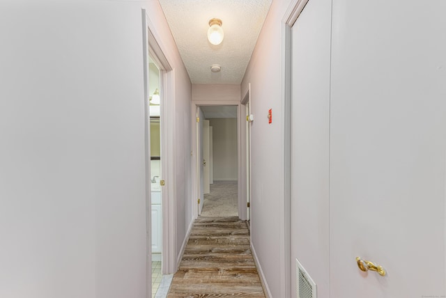 hall with visible vents, a textured ceiling, and baseboards