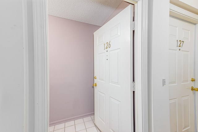 doorway featuring light tile patterned floors, a textured ceiling, and baseboards