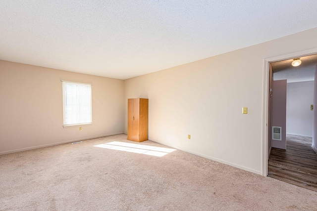 carpeted empty room featuring baseboards, visible vents, and a textured ceiling