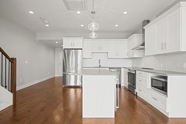 kitchen with a sink, appliances with stainless steel finishes, wall chimney range hood, a center island, and dark wood-style floors