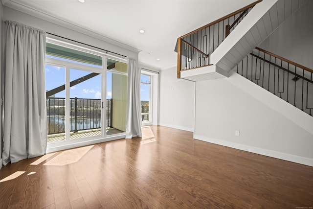 unfurnished living room with recessed lighting, wood finished floors, baseboards, ornamental molding, and stairway