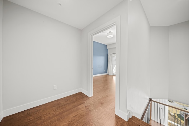 corridor with wood finished floors, an upstairs landing, and baseboards