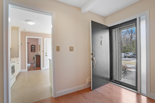 foyer entrance featuring light wood finished floors, beam ceiling, and baseboards