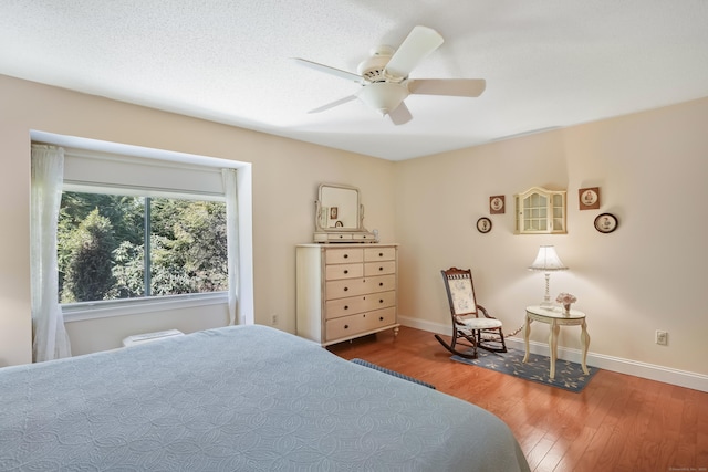 bedroom featuring ceiling fan, a textured ceiling, baseboards, and wood finished floors