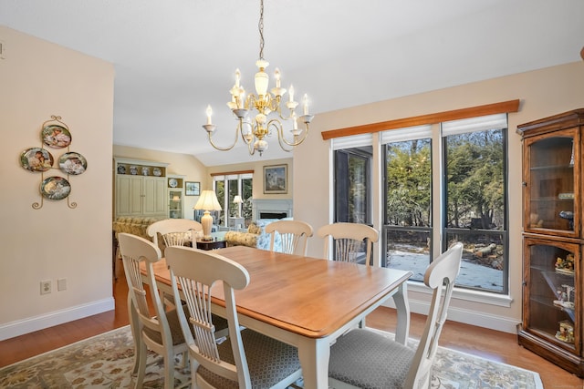 dining room with a fireplace, vaulted ceiling, wood finished floors, a chandelier, and baseboards