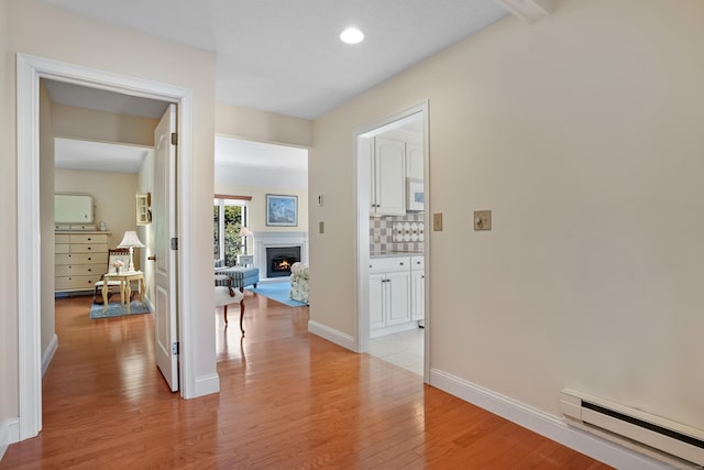 corridor featuring baseboard heating, light wood-style flooring, and baseboards