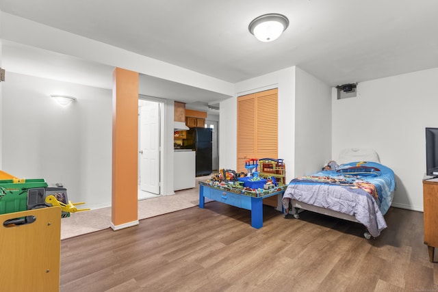 bedroom with a closet, wood finished floors, freestanding refrigerator, and baseboards