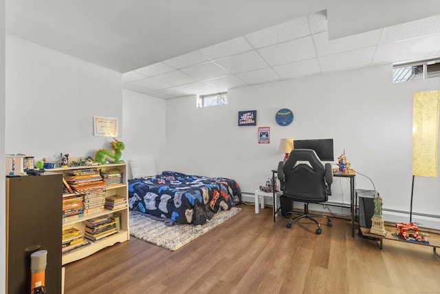 bedroom featuring a paneled ceiling, baseboard heating, and wood finished floors