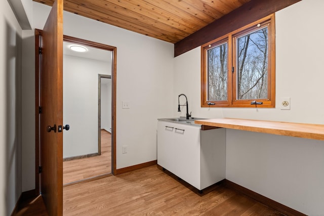 kitchen with light wood finished floors, baseboards, wooden ceiling, wooden counters, and a sink