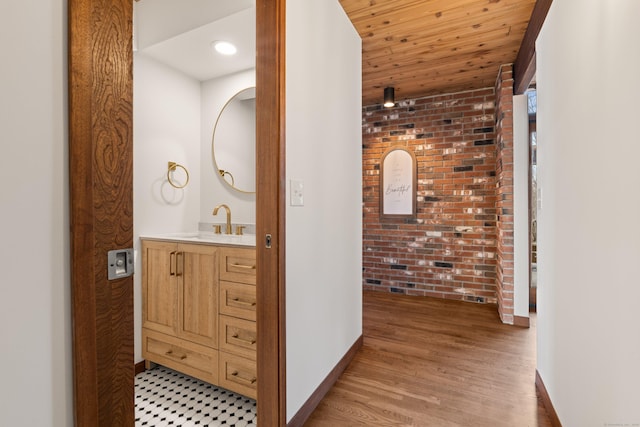 hallway featuring light wood finished floors, wood ceiling, a sink, brick wall, and baseboards