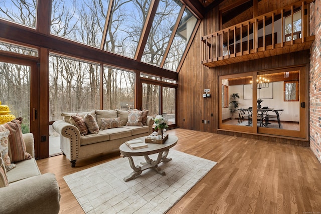 living area featuring a towering ceiling, a notable chandelier, wooden walls, and wood finished floors