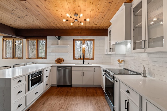 kitchen featuring tasteful backsplash, appliances with stainless steel finishes, light countertops, wall chimney range hood, and a sink