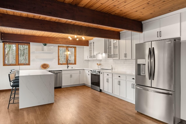 kitchen with tasteful backsplash, appliances with stainless steel finishes, glass insert cabinets, light wood-type flooring, and a sink