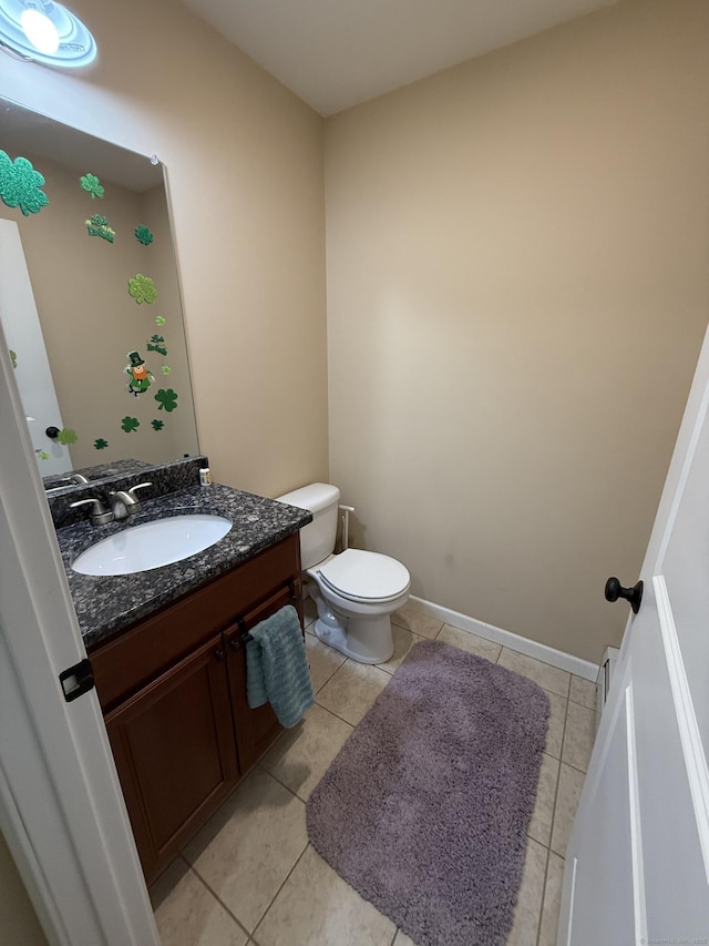 half bath featuring tile patterned flooring, baseboards, vanity, and toilet