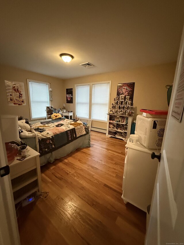 bedroom featuring light wood finished floors, multiple windows, and baseboard heating