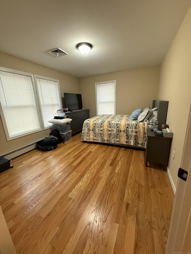 bedroom featuring a baseboard radiator, wood finished floors, visible vents, and baseboards