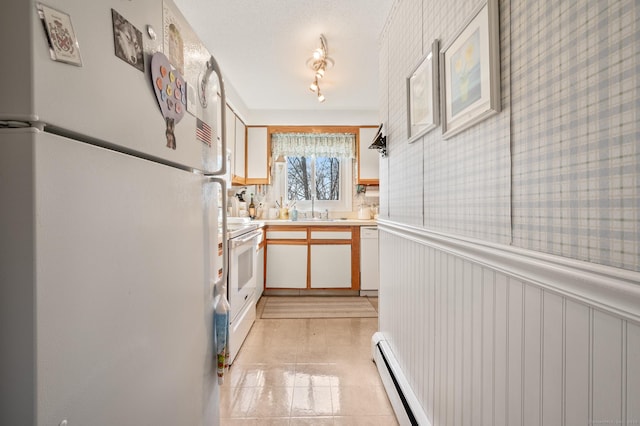 kitchen featuring a wainscoted wall, a baseboard heating unit, white appliances, light countertops, and wallpapered walls