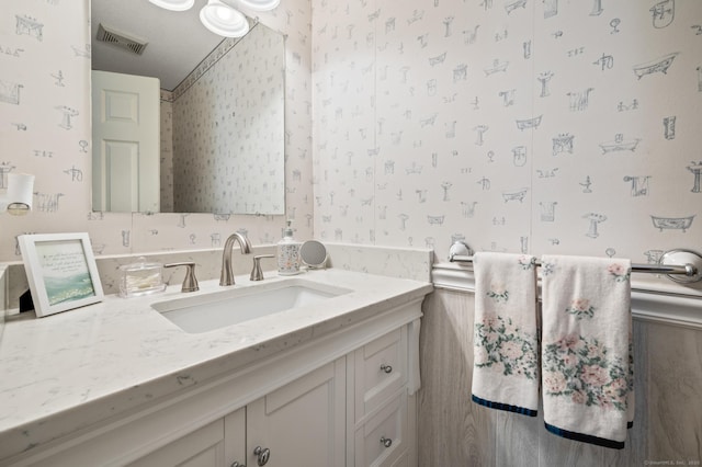 bathroom with visible vents, vanity, and wallpapered walls