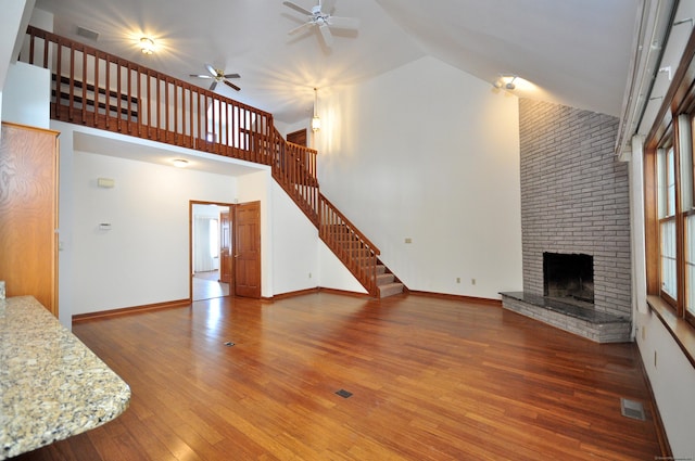 unfurnished living room featuring a fireplace, wood finished floors, a towering ceiling, visible vents, and stairs