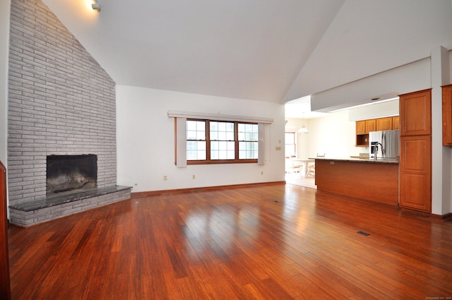 unfurnished living room featuring a brick fireplace, baseboards, high vaulted ceiling, and dark wood finished floors