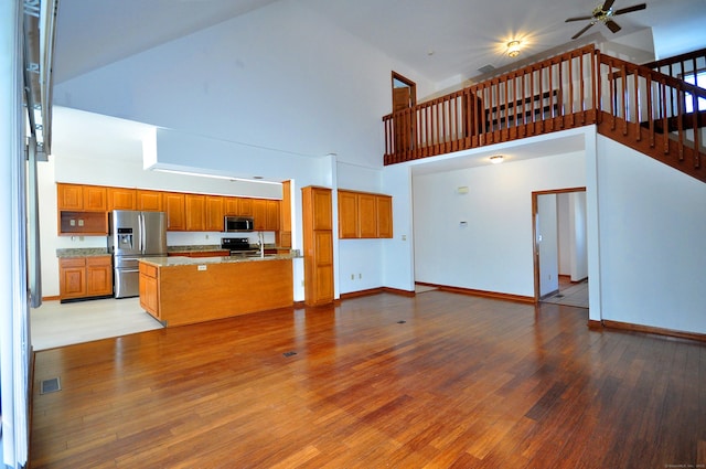 kitchen featuring open floor plan, appliances with stainless steel finishes, light wood-type flooring, and brown cabinets