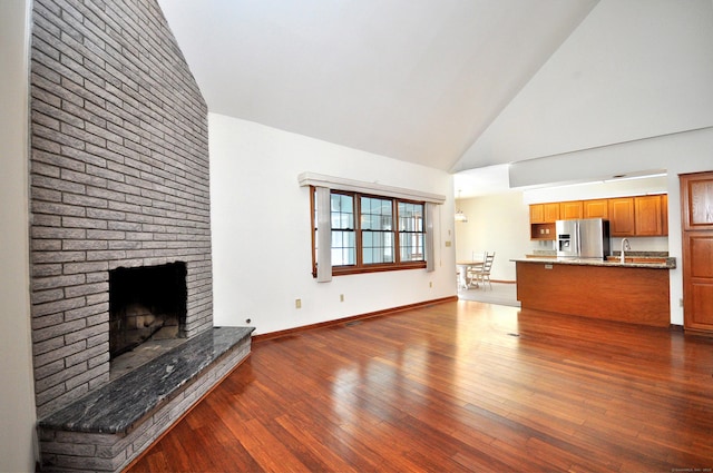 unfurnished living room featuring baseboards, dark wood finished floors, a fireplace, high vaulted ceiling, and a sink