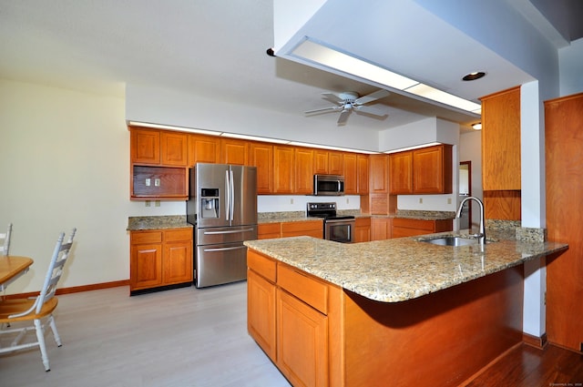 kitchen with appliances with stainless steel finishes, brown cabinetry, a sink, and light stone countertops